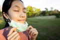 Happy smiling asian child girl is standing,taking off mask in green nature,breathe deep,woman enjoy breathing fresh air with