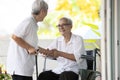 Happy smiling asian elderly woman sit in wheelchair and her old friend meeting at home and shaking hands,disabled senior people Royalty Free Stock Photo