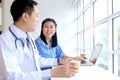 Happy smiling Asian female doctor taking break, drinking coffee during talking with teammate. Relaxed carefree medical staff Royalty Free Stock Photo