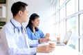 Happy smiling Asian female doctor taking break, drinking coffee during talking with teammate. Relaxed carefree medical staff Royalty Free Stock Photo