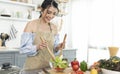 Happy smiling asian housewife in apron cooking salad in kitchen. woman healthy cooking concept Royalty Free Stock Photo