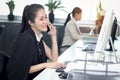 Happy smiling Asian woman officer sitting, talking on mobile phone at office desk with blurred busy colleague background, modern Royalty Free Stock Photo