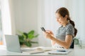 Happy smiling Asian woman relaxing using a smartphone to talk and laptop computer in bedroom at home. creative girl concept study Royalty Free Stock Photo