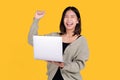 Happy smiling Asian woman wearing casual clothes is working on a laptop PC computer gesturing winner isolated on yellow background Royalty Free Stock Photo