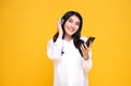 Happy smiling Asian woman wearing wireless headphones listening to music with smartphone on bright yellow background