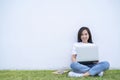 Happy smiling asian woman working on laptop computer while sitting on the grass floor with legs crossed Royalty Free Stock Photo