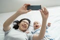 Happy Smiling Asian Young mother and her little cute baby boy lying on bed taking selfie photos with smartphone together Royalty Free Stock Photo