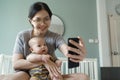 Happy Smiling Asian Young mother and Little Cute baby boy doing online video call with family on mobile phone at home. Mom and son Royalty Free Stock Photo