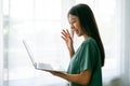 Happy smiling asian young woman using work laptop and standing beside window Royalty Free Stock Photo
