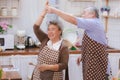 Happy & smiling attractive elderly cute Asian couple in love enjoying cooking healthy salad & dancing in kitchen at home together Royalty Free Stock Photo