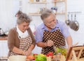 Happy & smiling attractive elderly cute Asian couple in love enjoying cooking healthy salad in kitchen at home together. Happiness
