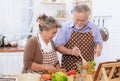 Happy & smiling attractive elderly cute Asian couple in love enjoying cooking healthy salad in kitchen at home together. Happiness Royalty Free Stock Photo