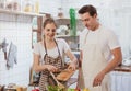 Happy & smiling attractive young cute caucasian couple in love enjoying cooking healthy salad in kitchen at home together.