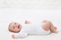 Happy Smiling Baby lying on back in White Bed. Active Playful Baby Boy in White Cotton Bodysuit. Laughing Infant Child in Onesies Royalty Free Stock Photo