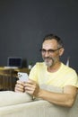 Happy smiling beard man using smartphone device while sitting on sofa at home. Mature man sitting on couch reading Royalty Free Stock Photo