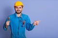 Happy and smiling bearded engineer with wrench tool in hand looking at camera and pointing aside with index finger while stands Royalty Free Stock Photo