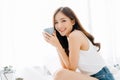 Happy smiling beautiful Asian woman awaking with cup of coffee and looking at camera in the bedroom. Lazy day off concept