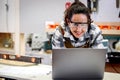 Happy smiling beautiful carpenter woman wearing safety glasses goggles and apron working on laptop computer, female craft worker Royalty Free Stock Photo