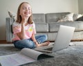 Happy smiling beautiful child girl 8 years old sitting on a gray carpet in front of a laptop, homework and online education Royalty Free Stock Photo
