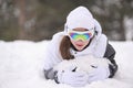 Happy smiling beautiful little girl in woolen hat and ski goggles wearing gloves lying in white snow during alpine mountain forest Royalty Free Stock Photo