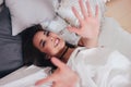 Happy smiling beautiful long hair asian girl young woman lying down in bed and pulling hands towards camera, cozy morning Royalty Free Stock Photo