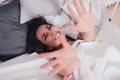 Happy smiling beautiful long hair asian girl young woman lying down in bed and pulling hands towards camera, cozy morning Royalty Free Stock Photo