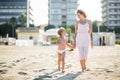 Happy smiling beautiful mom goes hand in hand with cute child at the beach