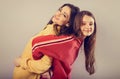 Happy smiling beautiful mother and cute playful daughter hugging in fashion trendy hoodie together on studio background with empty