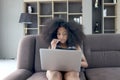 Happy smiling beautiful teenage girl with curly hair using laptop computer watching videos or movie and eating snacks while Royalty Free Stock Photo