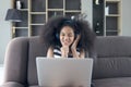 Happy smiling beautiful teenage girl with curly hair wearing headphones, using laptop computer for practicing to sing song while Royalty Free Stock Photo