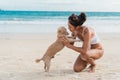 Happy smiling beautiful woman playing with her cute dog on the beach. Young Asian girl in swimwear hugging her pet on Royalty Free Stock Photo