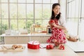 Happy smiling beautiful young Asian woman in red heart apron holds red coffee mug while stands behind kitchen counter. Girl Royalty Free Stock Photo