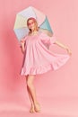 Happy smiling beautiful young girl in pink dress posing with colorful umbrella over pink studio background. Summertime Royalty Free Stock Photo