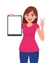 Happy smiling beautiful young woman holding / showing a blank clipboard and gesture hand victory, V or peace sign. Royalty Free Stock Photo