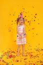 Happy smiling birthday child girl in pink cup surrounded by flying confetti on colored yellow background . Celebration Royalty Free Stock Photo