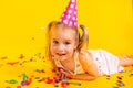 Happy smiling birthday child girl in pink cup surrounded by flying confetti on colored yellow background . Celebration Royalty Free Stock Photo