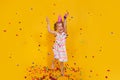 Happy smiling birthday child girl in pink cup surrounded by flying confetti jumping on colored yellow background Royalty Free Stock Photo