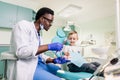 Happy smiling black dentist tells Caucasian little boy how to brush his teeth. Caries prevention, Dentistry, teeth