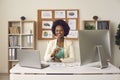 Happy smiling black woman sitting at office desk with laptop and desktop computer