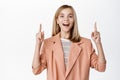 Happy smiling blond little girl, child in suit blazer pointing fingers up, showing advertisement, standing over white Royalty Free Stock Photo