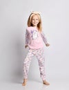 Happy smiling blonde kid girl with headband and in stylish shirt and pants pyjamas with flower print pattern is posing