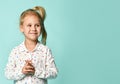 Little blonde schoolgirl with ponytail, in shirt with hearts print. Smiling, posing on blue background. Close up Royalty Free Stock Photo