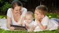 Happy smiling boy with baby brother and mother lying on grass in park and browsing internet on tablet computer Royalty Free Stock Photo