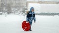 Happy smiling boy carrying plastic sleds up the hill before sliding down on a snowy day. Fun and joy on winter holidays, kids Royalty Free Stock Photo