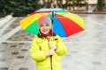 Happy smiling boy enjoying rain in city. Kid has colorful rainbow umbrella. Child wears waterproof warm jacket. Autumn rainy