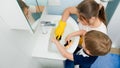 Happy smiling boy with mother wearing rubber gloves applying detergent and cleanser on sponges and washing bathroom