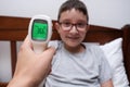 A happy smiling boy with normal temperature that is shown on a display of infrared contactless thermometer, concept pf