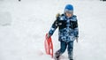 Happy smiling boy walking up the snowy hill with his plastic sleds at snowfall. The concept of children having fun during winter, Royalty Free Stock Photo