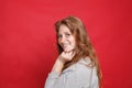 Happy smiling brunette woman in grey sweater standing sideways on red studio wall background Royalty Free Stock Photo