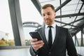 Happy smiling businessman wearing black suit and using modern smartphone near office at early morning, successful Royalty Free Stock Photo